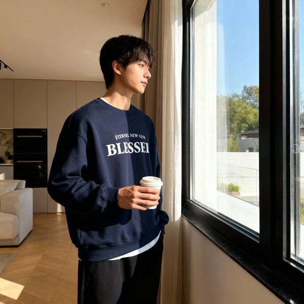 Person wearing a navy blue sweatshirt with 'BLESSED' text, holding a cup by a window.